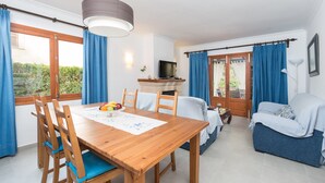 A dining area with a wooden table and chairs, a television on a stand, and a sofa in the living area. - CAN CAIMARI - Chalet for 6 people in Bonaire. (Mal Pas-Bon Aire)