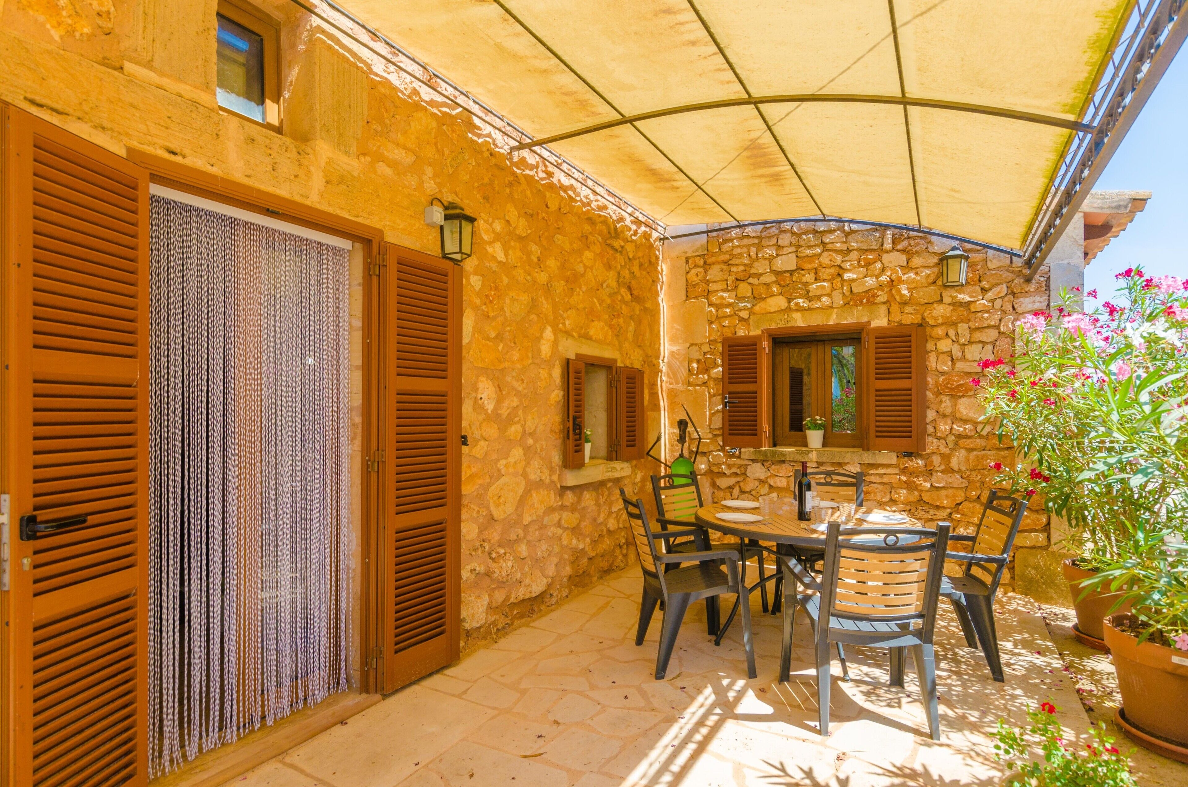 Un bâtiment en pierre doté d’un patio couvert, de volets en bois et d’une table avec des chaises.