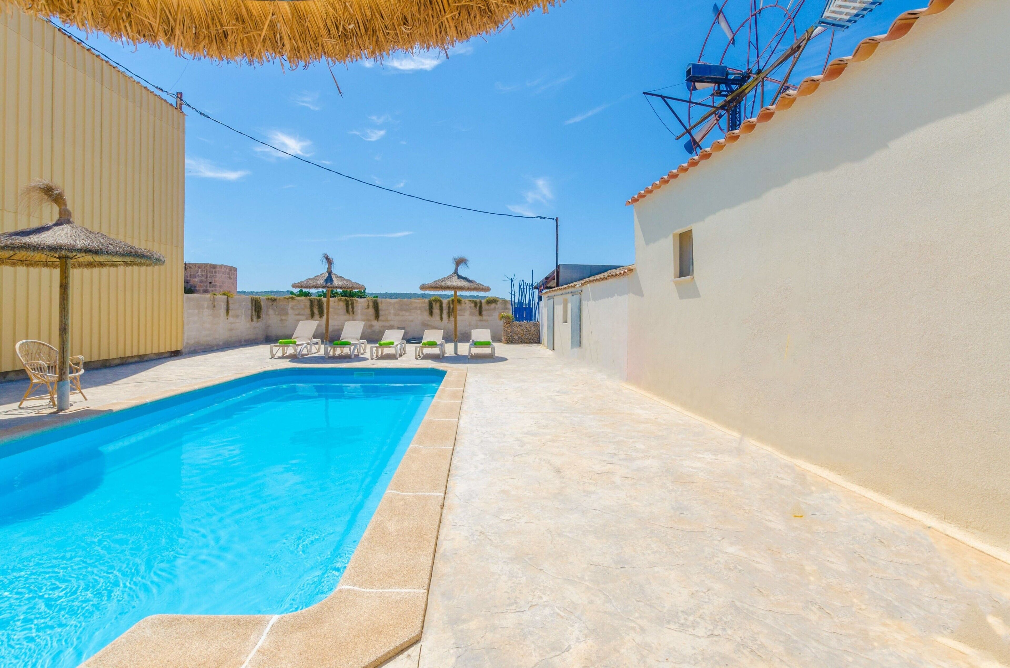 A swimming pool with lounge chairs and umbrellas, surrounded by a tiled patio and a building with a tiled roof.