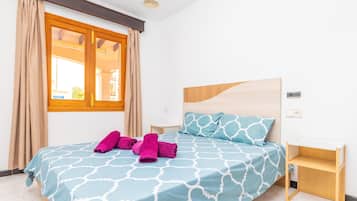 Une chambre à coucher avec un lit, une tête de lit en bois, une table de chevet et une fenêtre avec des rideaux.