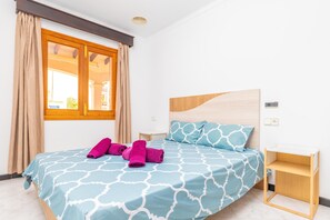 Une chambre à coucher avec un lit, une tête de lit en bois, une table de chevet et une fenêtre avec des rideaux.