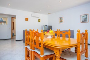 Un comedor con una mesa redonda de madera y sillas a juego, un cuenco de fruta y un televisor en la pared.