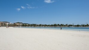 En bred sandstrand med en klarblå himmel och byggnader som syns i fjärran.