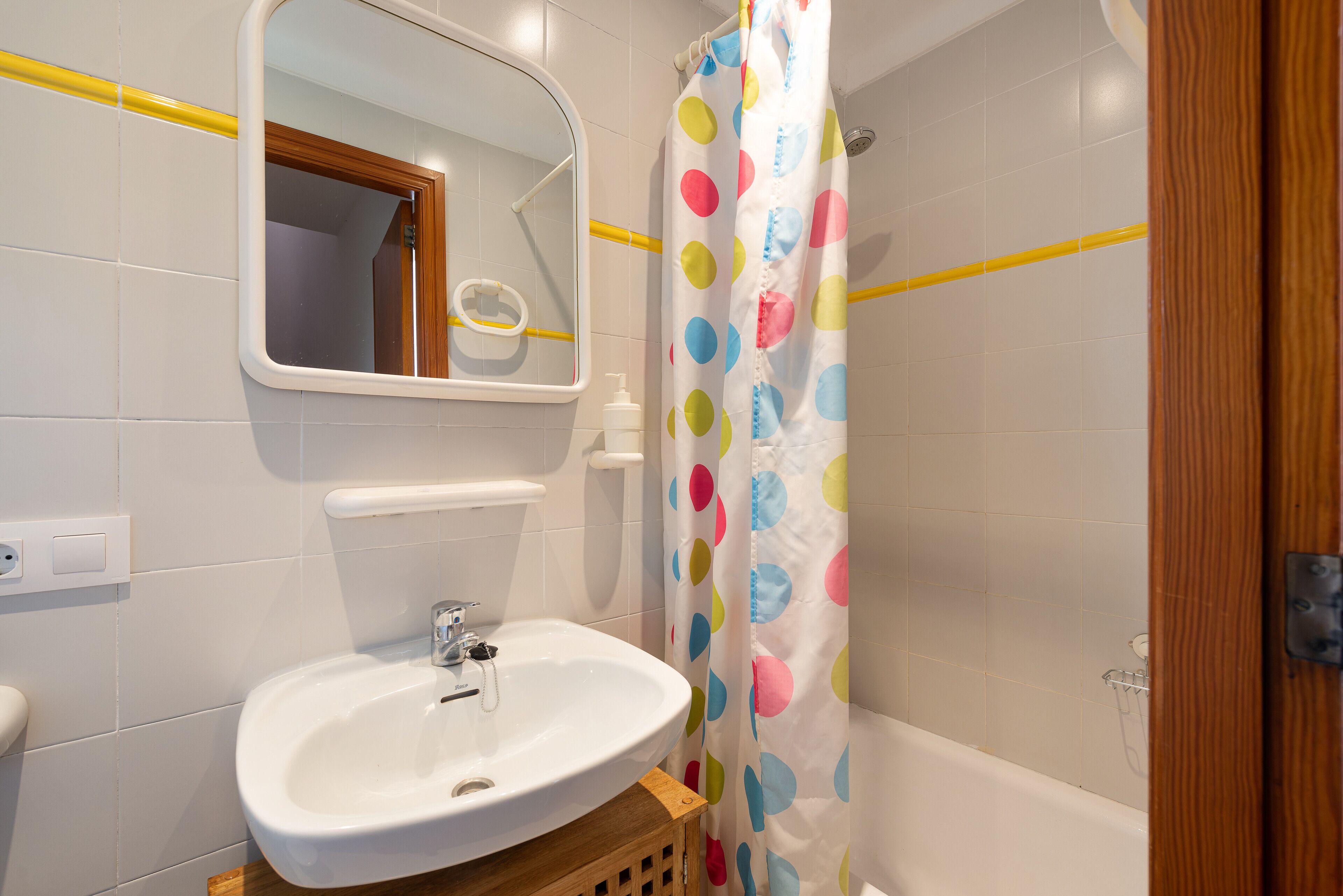 A bathroom with a white sink, mirror, and shower curtain with colorful polka dots.