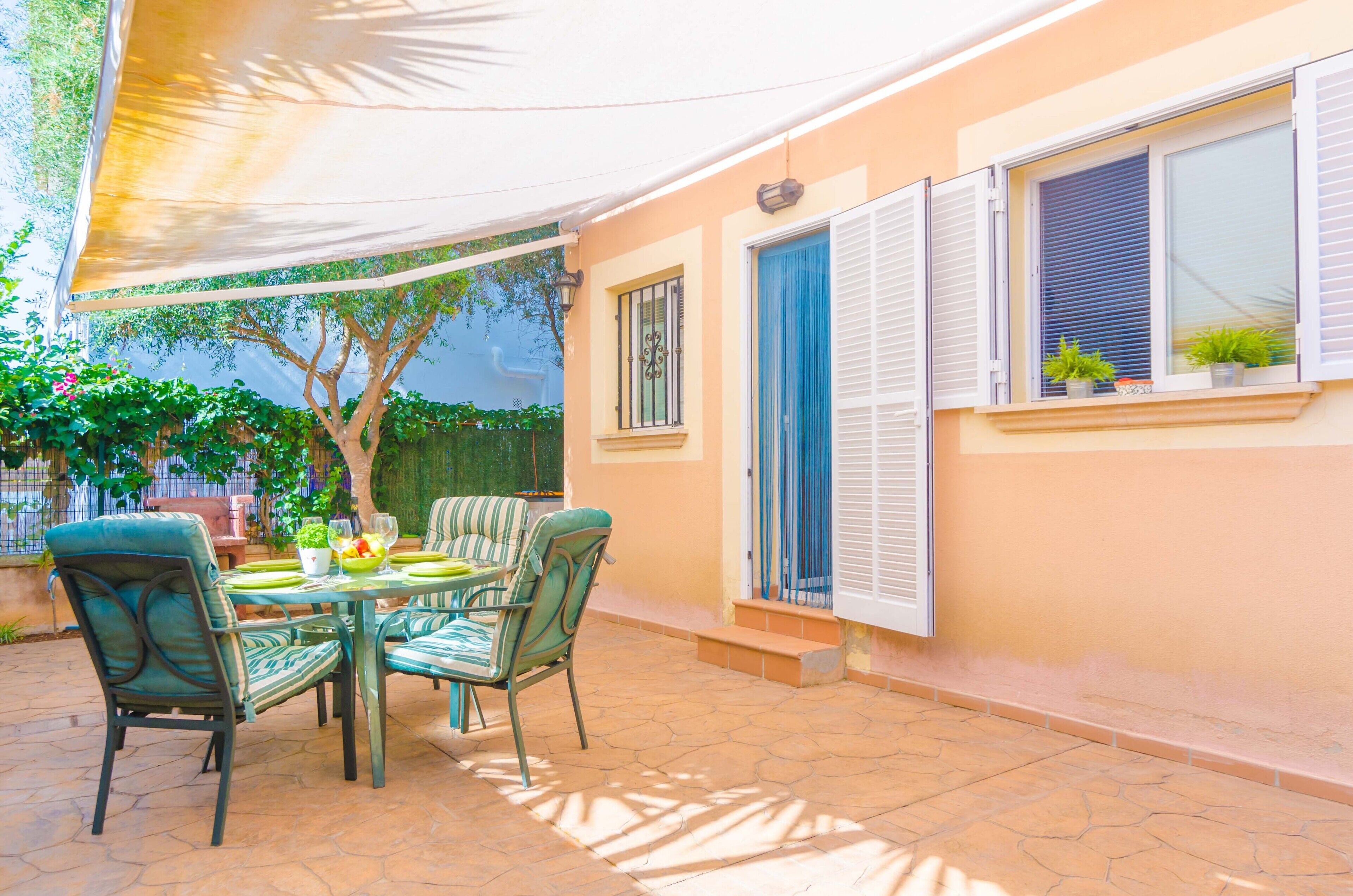 An outdoor patio with a table and chairs, a tree, and a building with windows and shutters.