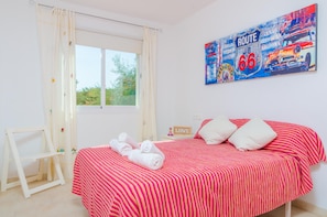 Una camera da letto con un letto, una finestra, un quadro e un tavolino con un cartello.