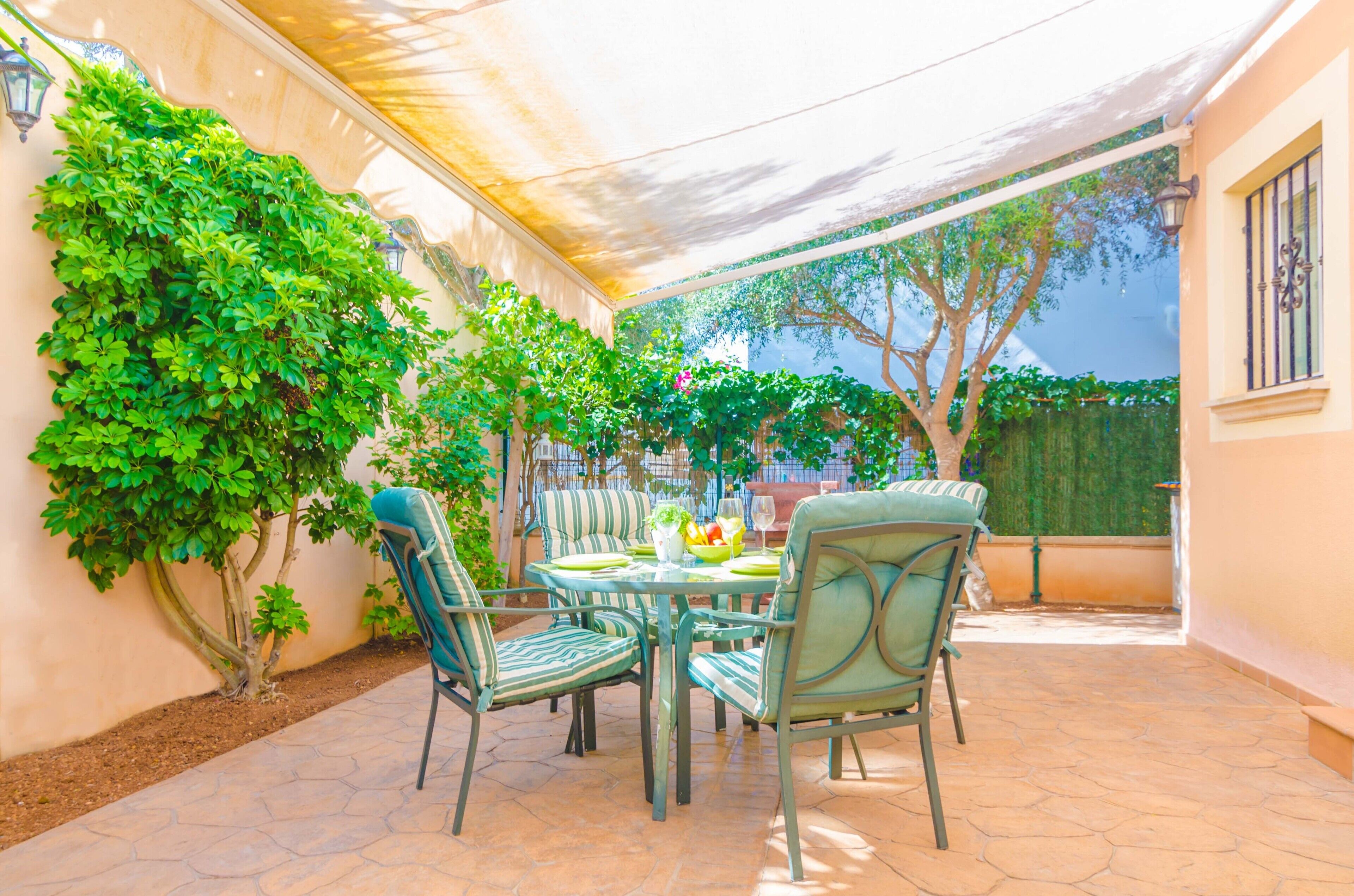 Een terras met een tafel en stoelen, omgeven door groen en een pergola.