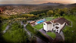 Ett flygbildsfoto av en villa med en swimmingpool, omgiven av frodig grönska och med en vacker utsikt över en stad och berg i fjärran.