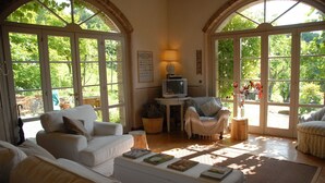 Un salón luminoso con un sofá blanco, una mesita con libros, un televisor y una silla.