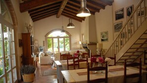 Un salón comedor espacioso con techo alto, sillas de madera y una mesa, y una escalera que lleva a un nivel superior.