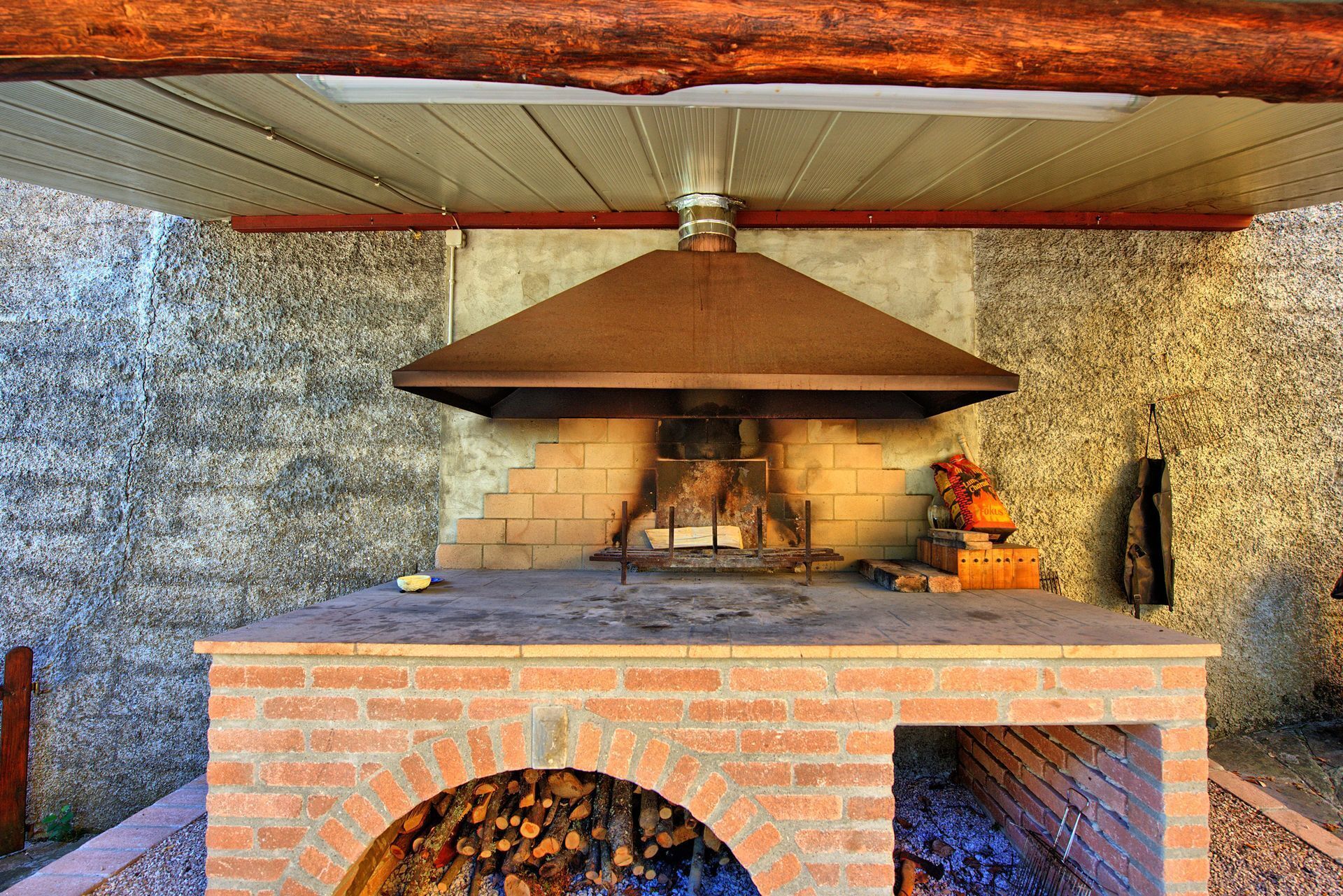 An outdoor brick oven with a chimney, a fire burning inside, and a bag of chips on the side.
