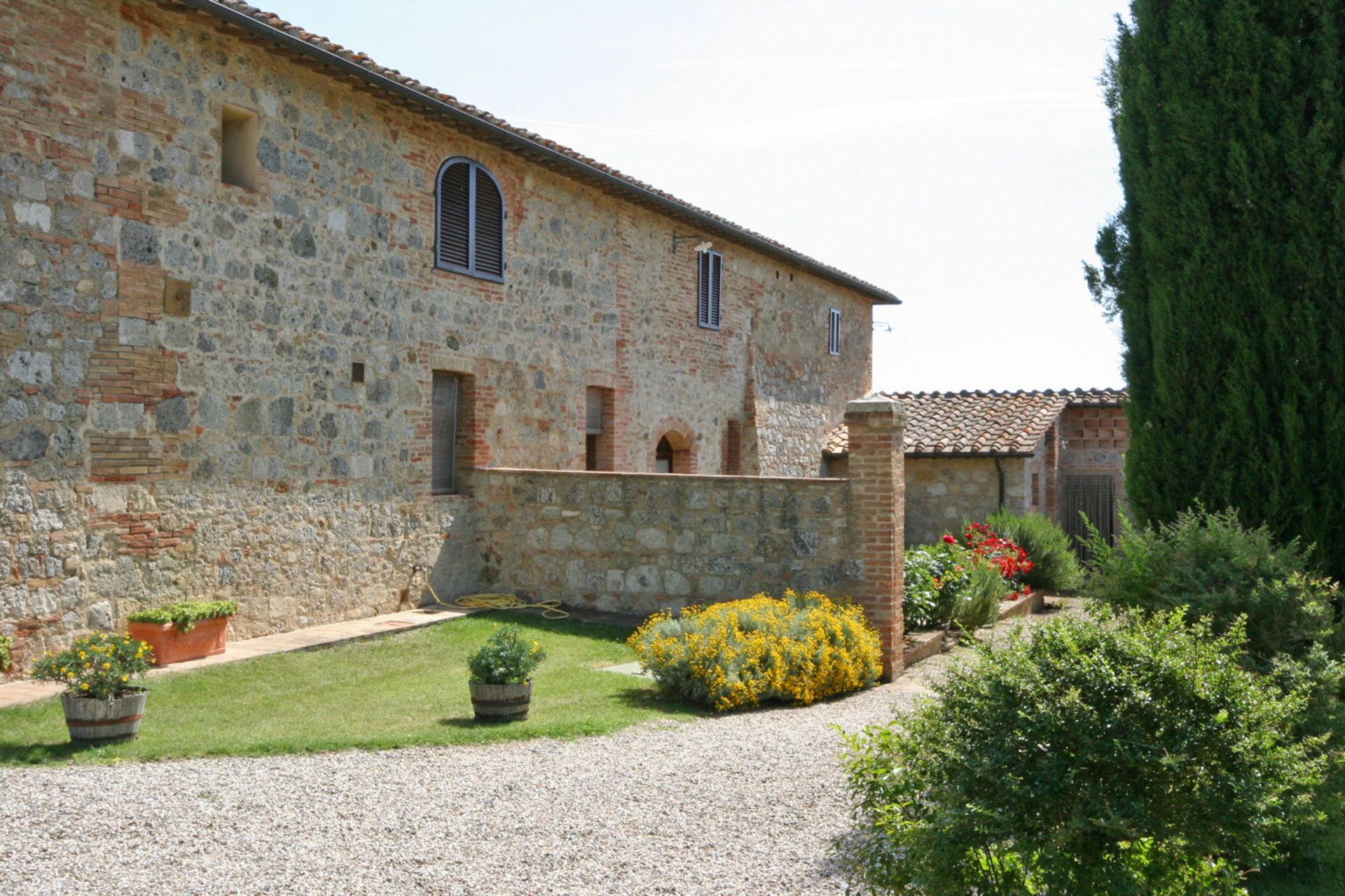 A stone building with a courtyard, a gravel path, and potted plants.