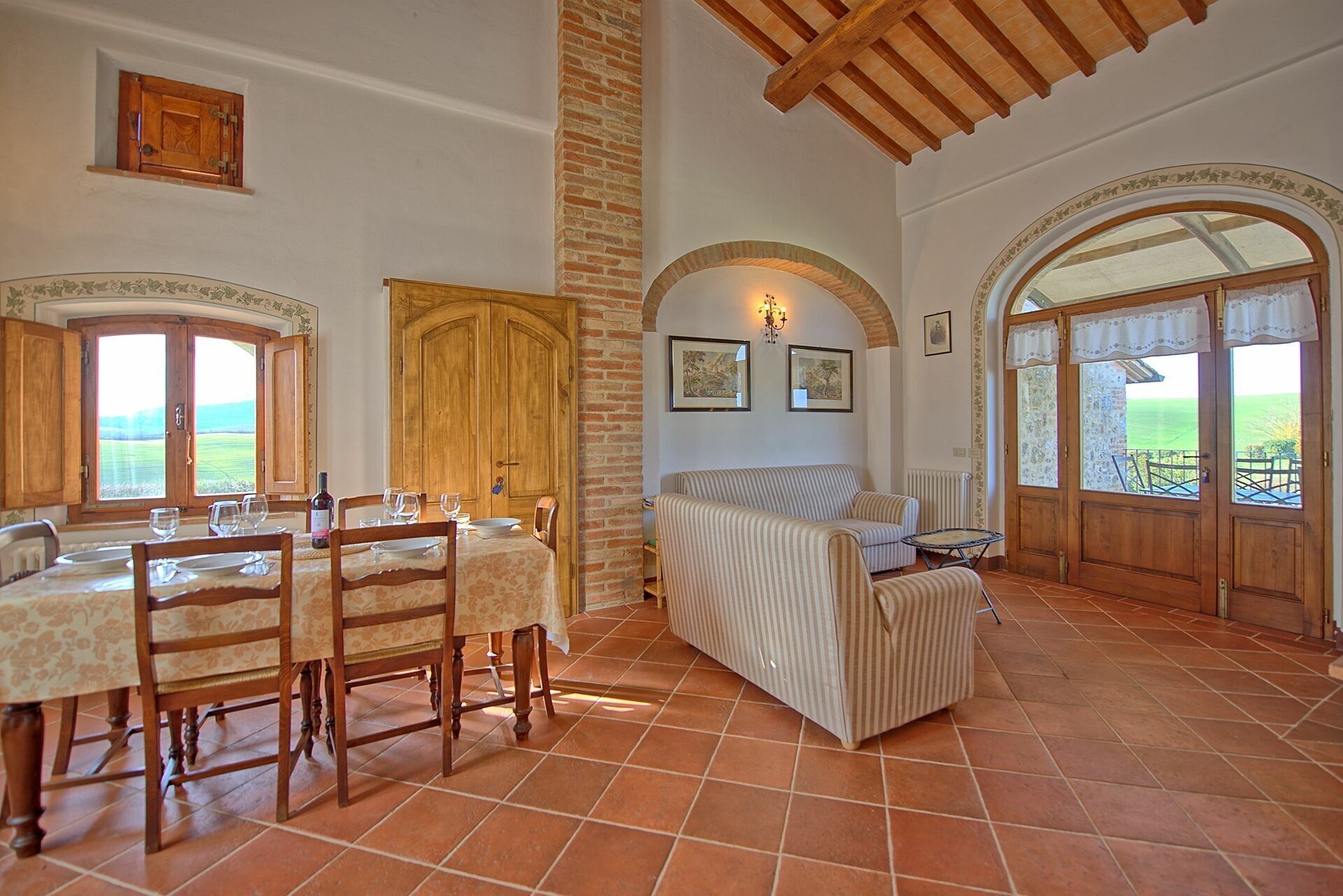 A dining area with a table set for four, a sofa, and a view of the outdoors through large windows.