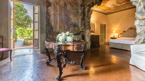 A room with a stone wall, a bed, a table with a vase of flowers, and a large window. - La Grotta - Apartment with swimming pool (Montespertoli)