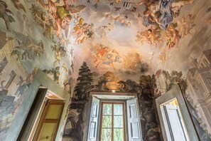 A room with a high ceiling featuring frescoes, a window with shutters, and a door with a wooden frame. - La Grotta - Apartment with swimming pool (Montespertoli)
