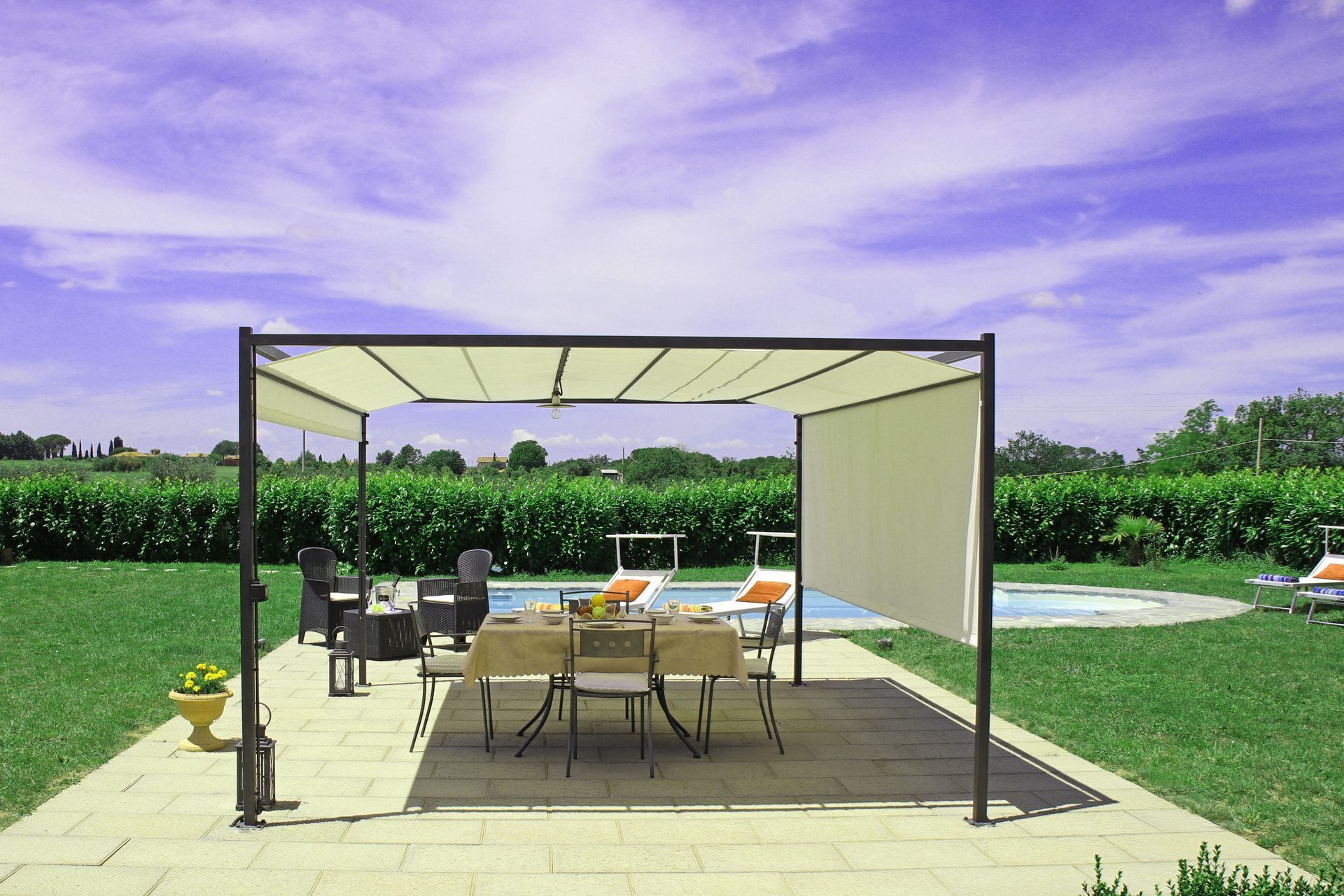 Un espacio al aire libre cubierto con una mesa, sillas, una piscina y un seto de fondo.