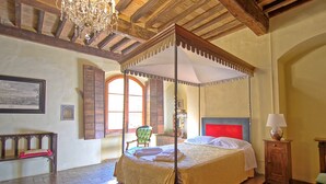 A four-poster canopy bed with a red headboard, a wooden bench, and a chandelier. - Montegufoni 24 - Apartment with swimming pool (Montespertoli)