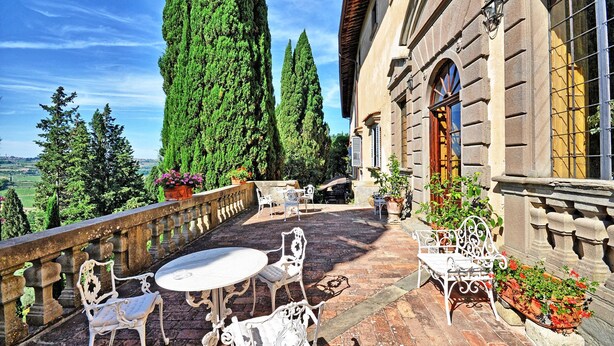 Eine Terrasse mit Gartenmöbeln, Steinbalustrade und Topfpflanzen.