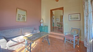 Un soggiorno accogliente con un divano, un tavolo e una poltrona. Si nota un soffitto in legno e una porta che dà su un'altra stanza.