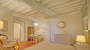 Ein Schlafzimmer mit einem großen Bett, einem Schminktisch, einem Sessel, einem Schreibtisch und einem Spiegel.