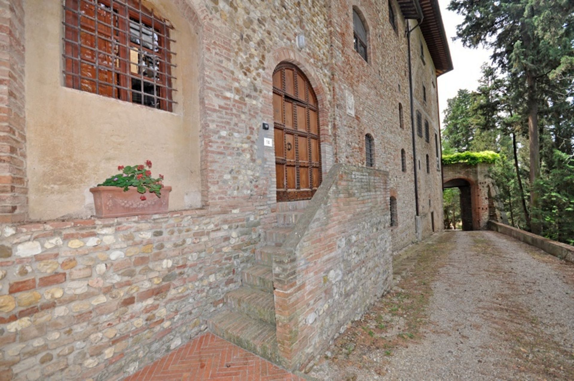Un edificio in pietra con una porta e una finestra in legno, un vialetto in mattoni e un piccolo vaso con fiori.