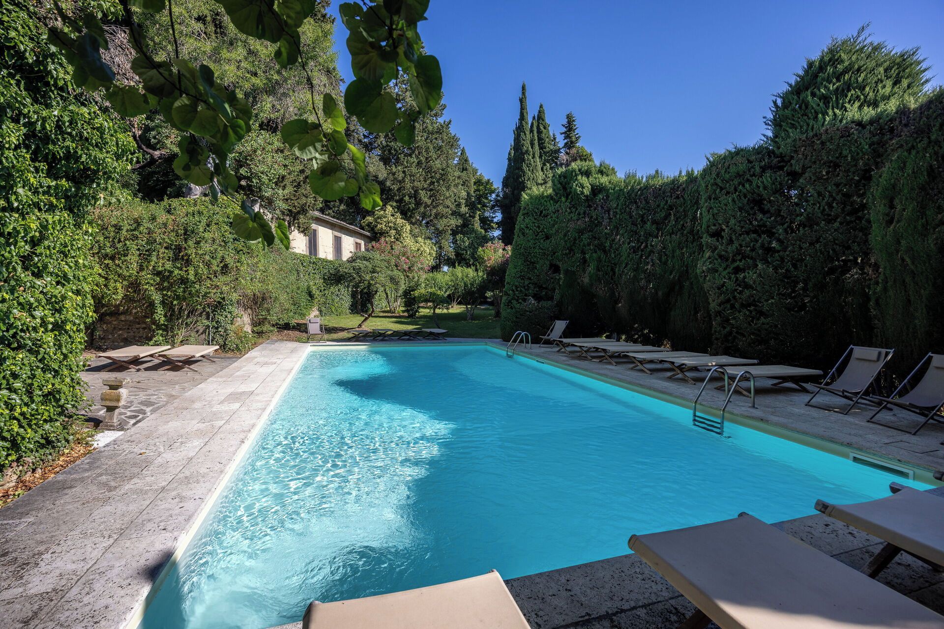 A swimming pool with lounge chairs, surrounded by greenery and a stone wall.