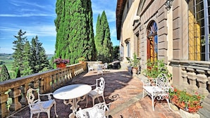 Une terrasse aménagée avec du mobilier d’extérieur, une balustrade en pierre et des plantes en pot.