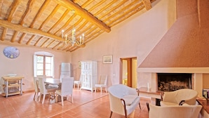 Un vaste salon doté d’un haut plafond en bois, d’une cheminée et d’un coin repas avec des chaises et une table.