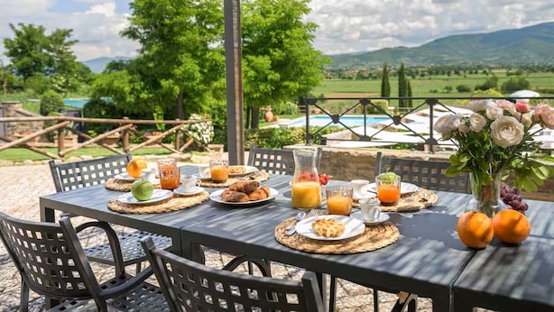 An outdoor dining table set with breakfast items, surrounded by chairs, with a scenic view of mountains and a pool in the background. - Villa Giare - Villa with private pool (Fratticciola)