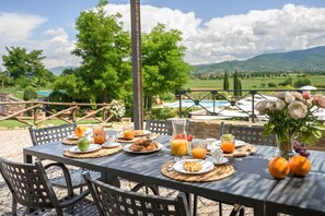 An outdoor dining table set with breakfast items, surrounded by chairs, with a scenic view of mountains and a pool in the background. - Villa Giare - Villa with private pool (Fratticciola)