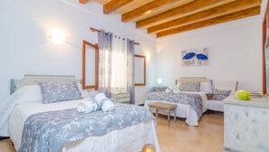 A bedroom with two beds, wooden beams on the ceiling, a bedside table with a lamp, and a wall-mounted artwork. - CAN PEDRO ROS - Lovely chalet with a terrace in s’Illot and free Wi-Fi (S'ILLOT)