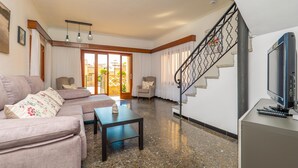 A living room with a sofa, a coffee table, a TV, and a staircase. - CAN PEDRO ROS - Lovely chalet with a terrace in s’Illot and free Wi-Fi (S'ILLOT)