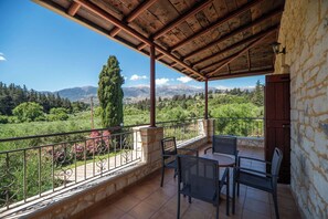 A covered outdoor area with a table and chairs, stone walls, and a view of mountains and greenery.