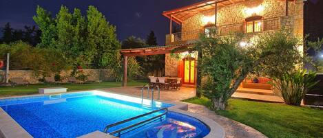 A stone house with a swimming pool, outdoor seating, and a covered patio area.