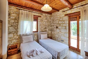 Habitación con dos camas, paredes de piedra, vigas de madera en el techo y vistas a la vegetación.