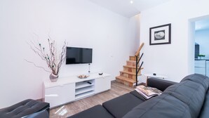 Ein modernes Wohnzimmer mit Flachbildfernseher, einer weißen Unterhaltungsanlage, einem schwarzen Sofa, einer Treppe und einem gerahmten Bild an der Wand.