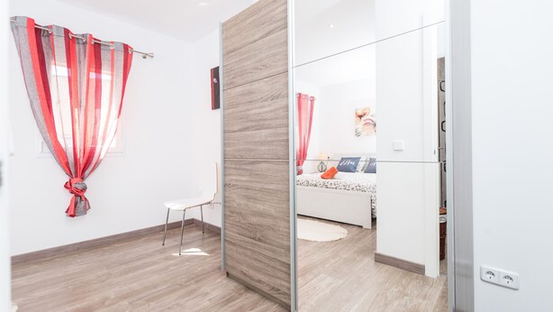 Ein modernes Schlafzimmer mit Schiebetür, einem Bett mit gemustertem Überwurf und einem kleinen weißen Sessel.