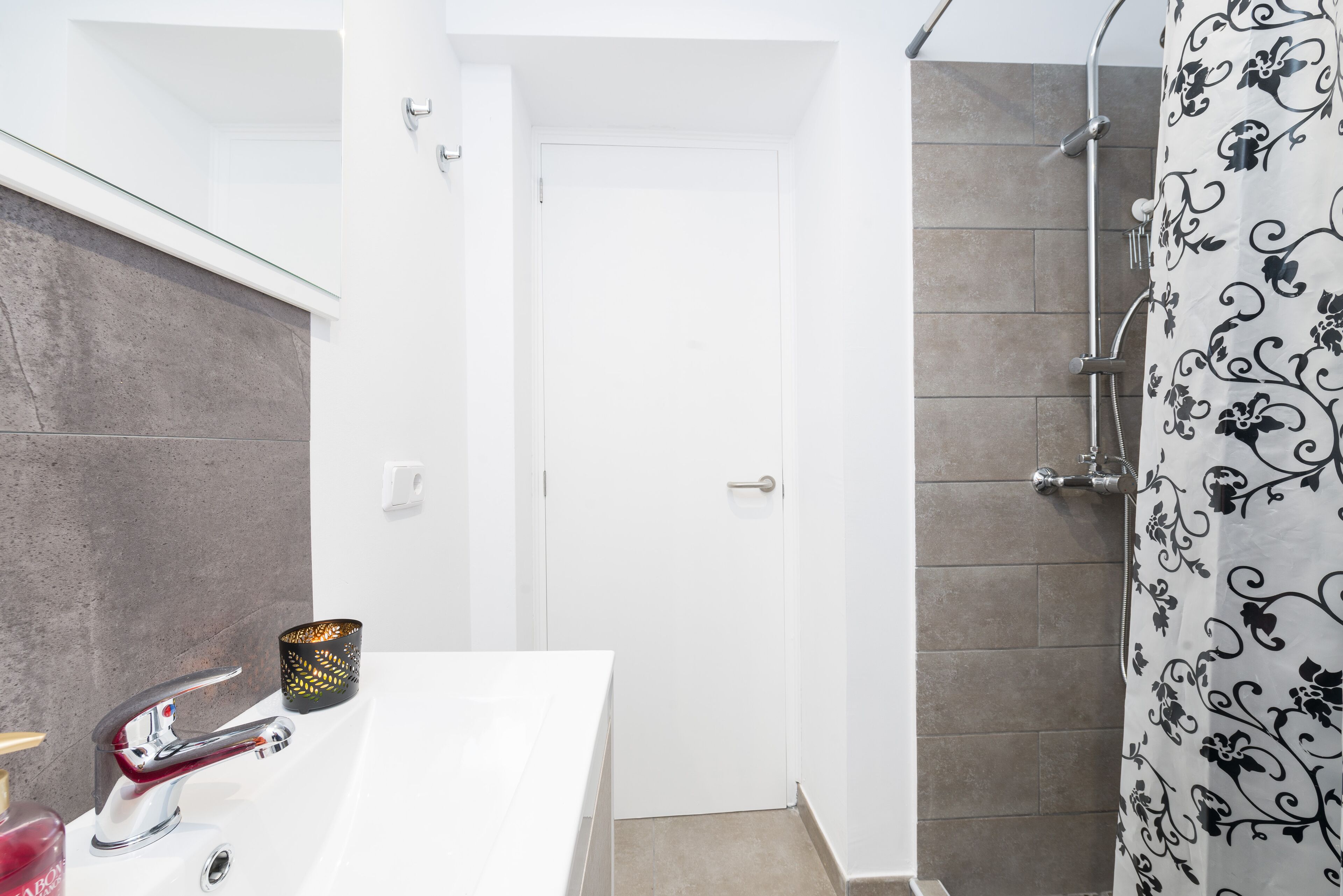 Un baño con un lavamanos blanco, una ducha con cortina de diseño blanco y negro, y una puerta que da a otra habitación.