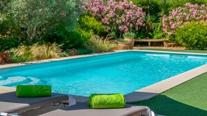 A swimming pool with a green towel on a lounge chair, surrounded by lush greenery and pink flowers. - CAS PILOT - Villa with private pool in Santa Maria del Cami. Free WiFi (Santa Maria)