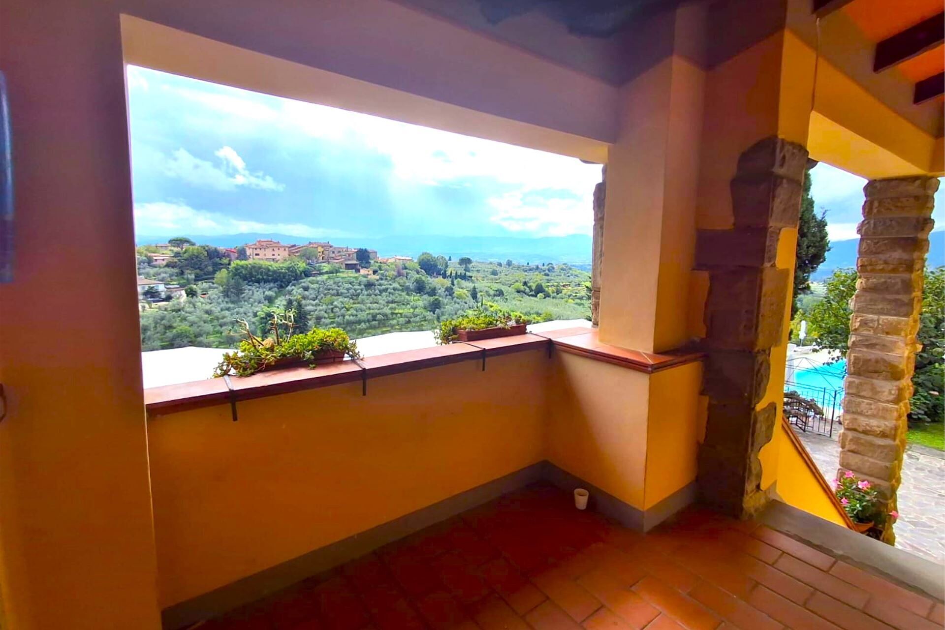 Ein Balkon mit Blick auf ein Hügel-Dorf und eine Steinsäule.
