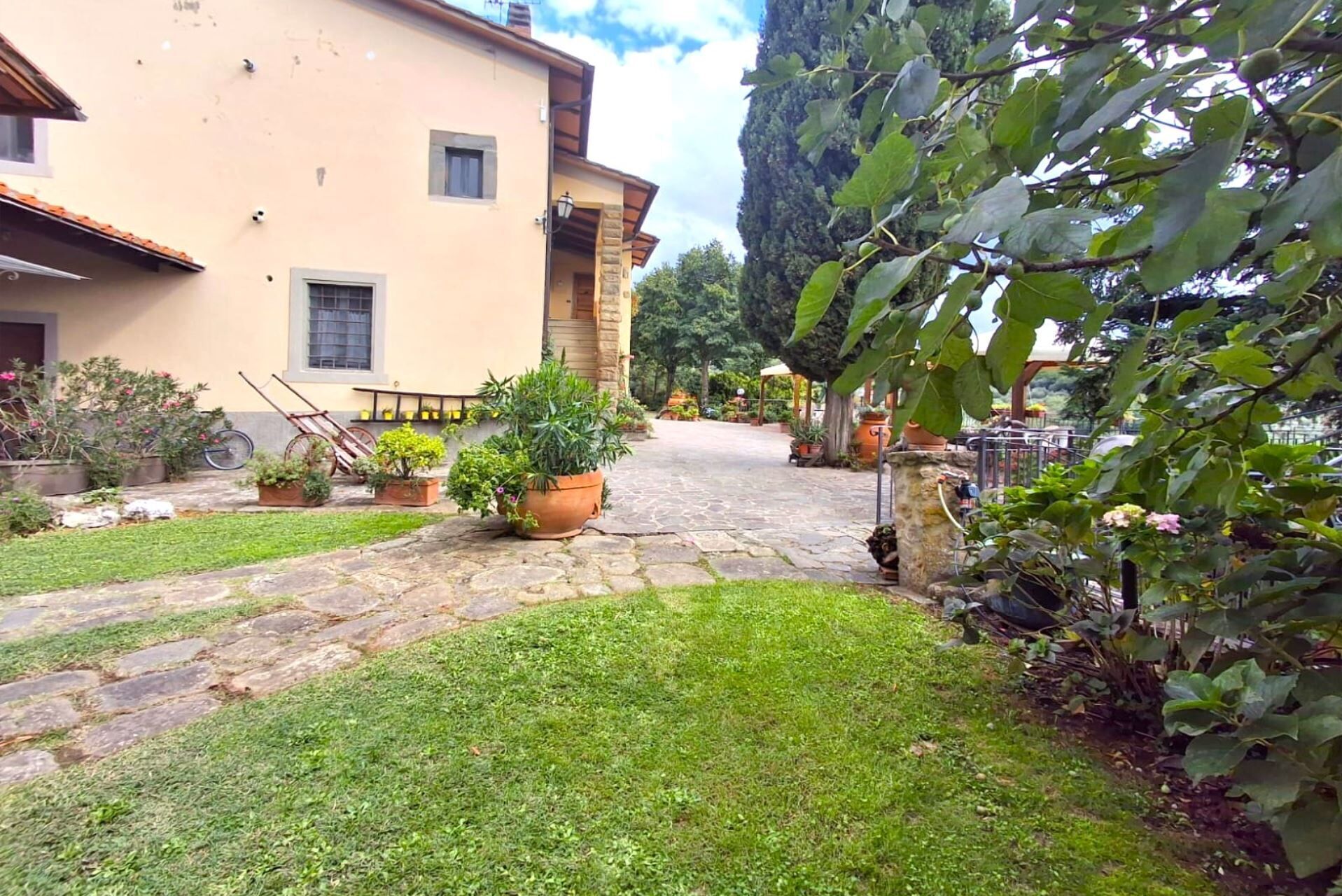 Un patio con un sendero de piedra que lleva a un edificio con tejado de baldosas. Hay plantas en macetas y una bicicleta en primer plano.