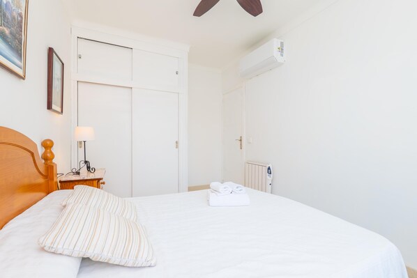 A neatly made bed with a pillow, a bedside table with a lamp, a radiator, and a door.