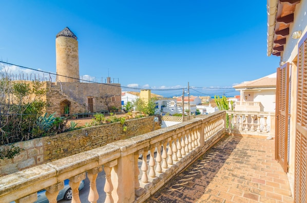A balcony with stone railings overlooking a historic tower and a stone wall with vegetation.