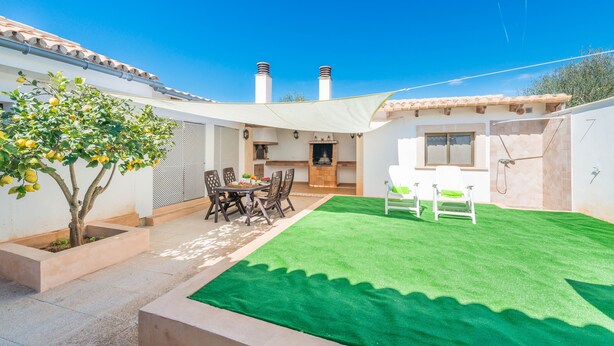 Eine Terrasse mit Esstisch, Stühlen, einem kleinen Baum und einem grünen Rasen aus Kunststoff.