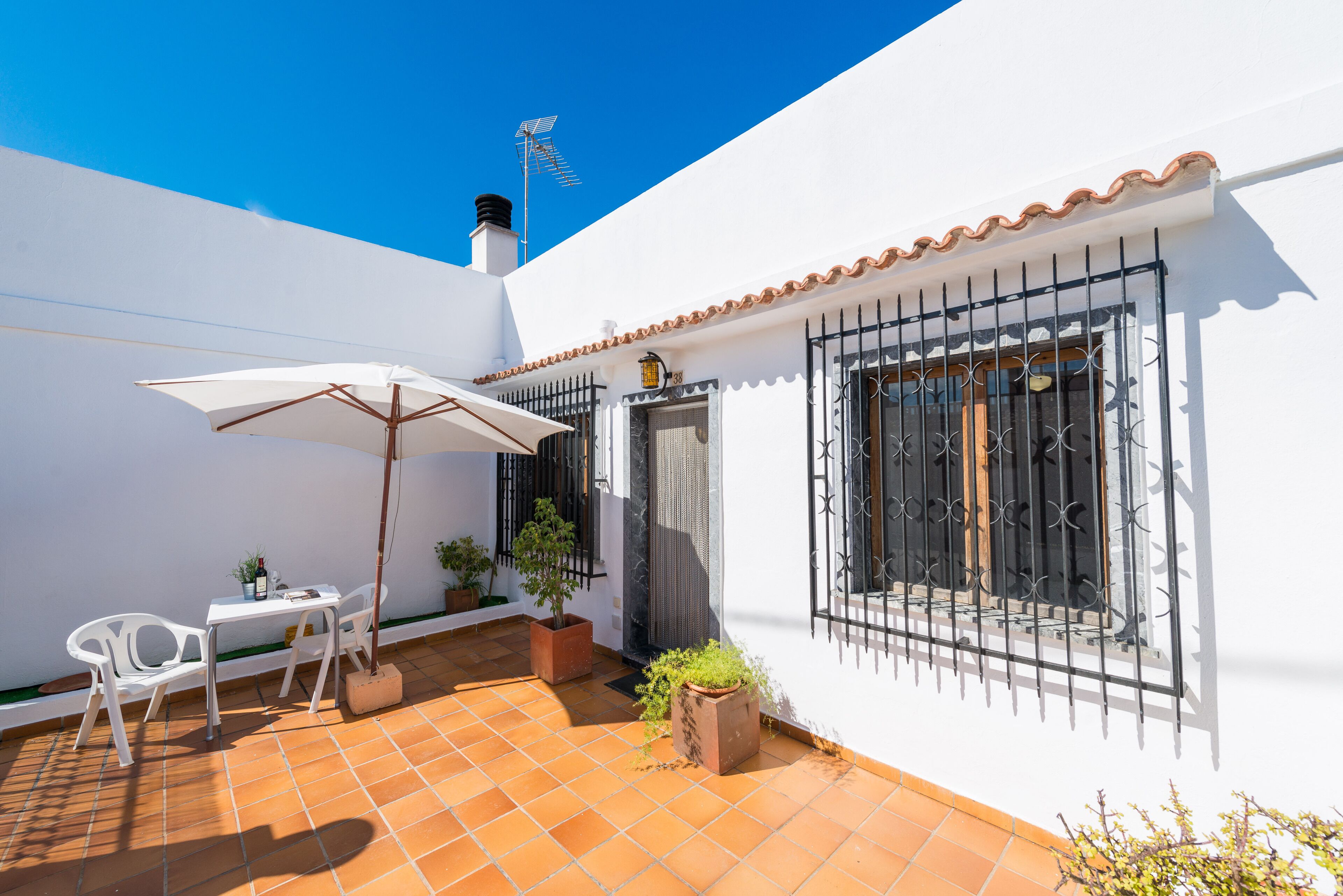 A patio with a white table and chairs, a white umbrella, and potted plants.