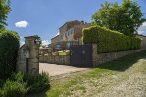 A stone building with a paved entrance, a gated area, and a well-maintained hedge.
