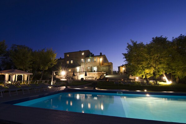 A large building with a swimming pool, surrounded by trees and outdoor seating.
