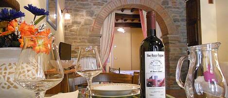 A dining table set with wine glasses, a bottle of wine, and a pitcher, with a stone wall and wooden beams in the background.