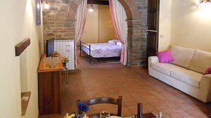 A room with a stone archway, a bed with a canopy, a white sofa, a wooden table with a vase, and a radiator. - Nice apartment for 2 people with WIFI and TV (Cortona)
