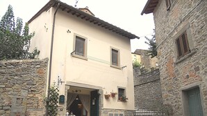 A two-story building with a stone facade, a balcony, and a small shop at the entrance. - Nice apartment for 2 people with WIFI and TV (Cortona)